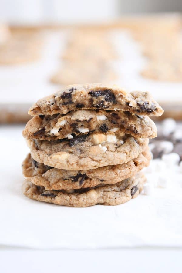 A stack of S'Mores chocolate chip cookie on parchment lined baking tray with the top cookie split in half.