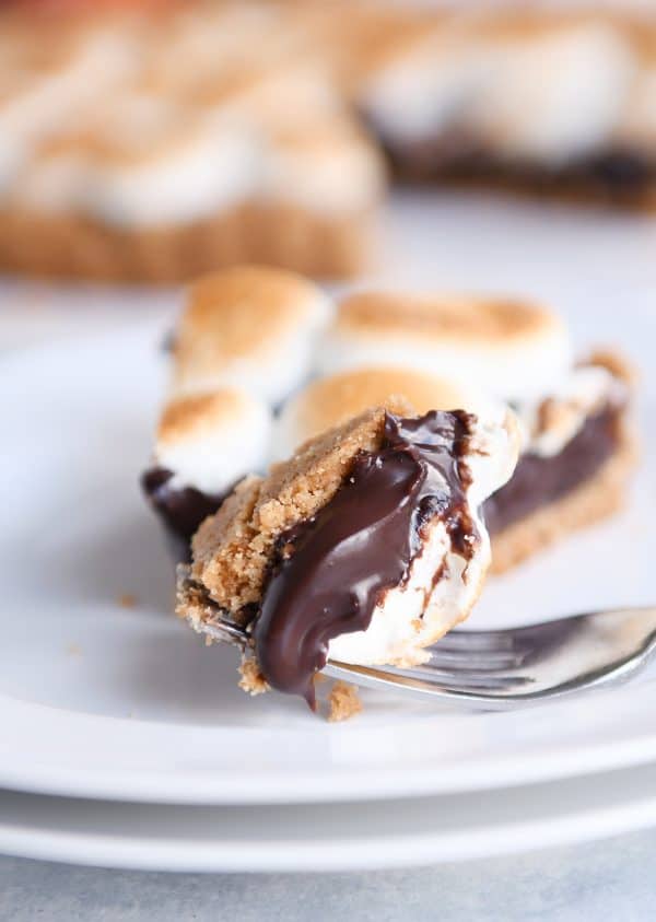 Bite taken out of s'mores pie on white plate with bite on fork.