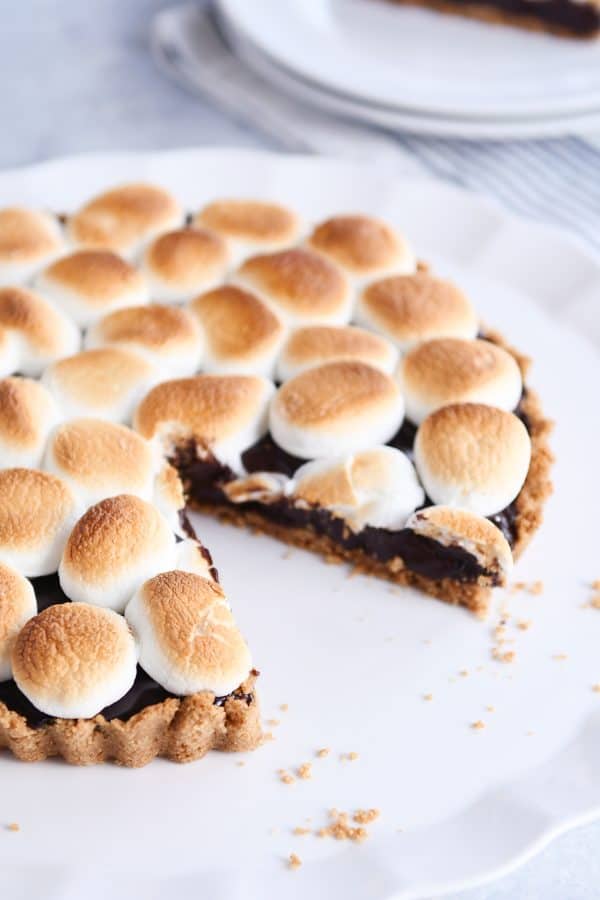 Slice taken out of full s'mores pie on white platter.