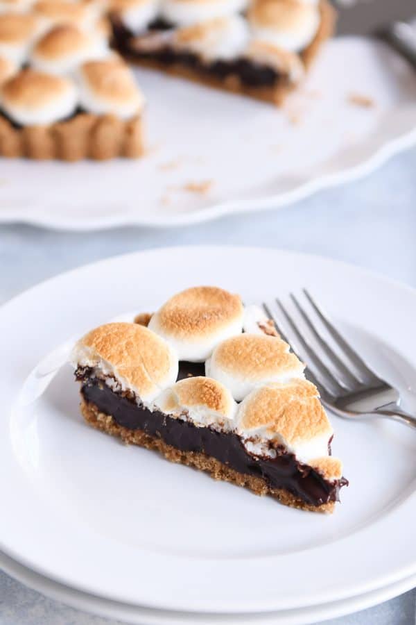 Piece of s'mores pie on white plate with fork.