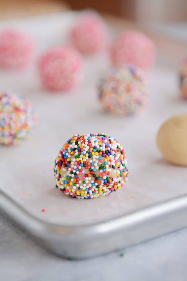 Sugar cookie balls coated with sprinkles on a cookie sheet. 