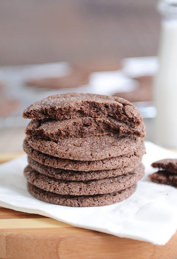 Stack of chocolate sugar cookies on a white napkin with one cookie broken in half.