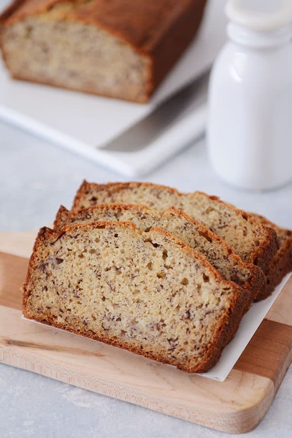 A loaf of banana bread with three slices cut out and stacked in front of the rest of the loaf.