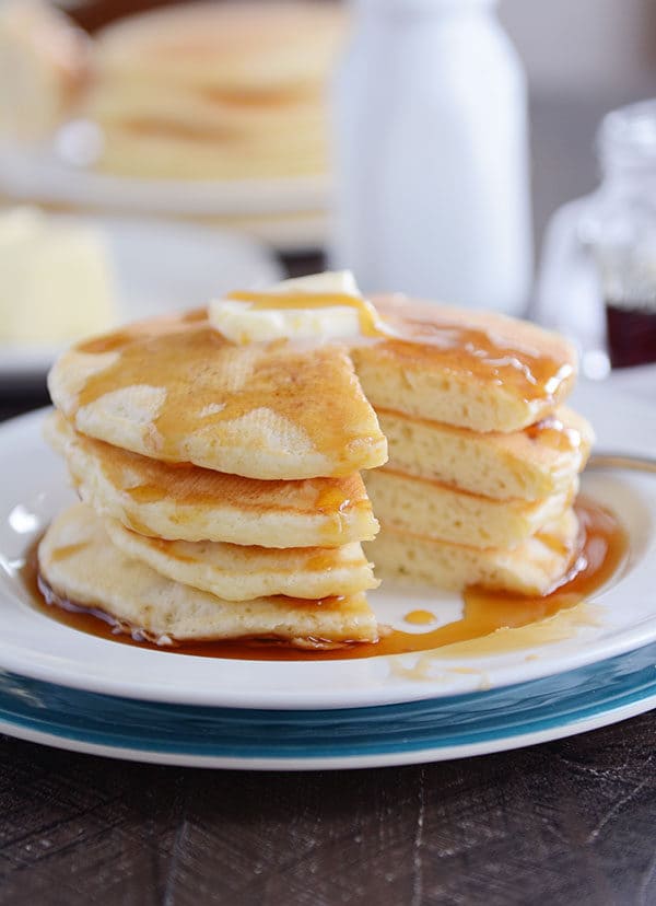 A stack of fluffy pancakes on a white plate topped with syrup and a pat of butter.