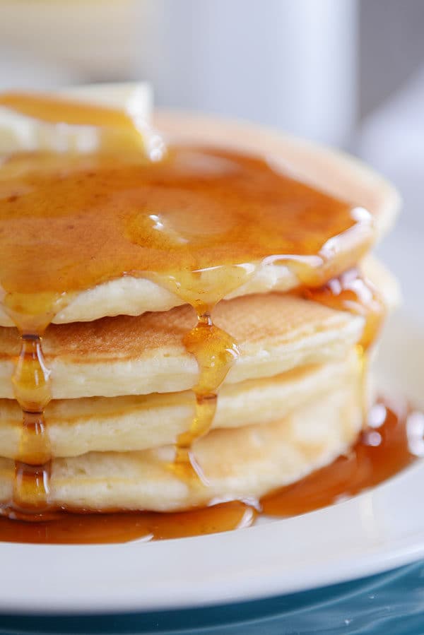 A stack of pancakes with syrup dripping down the sides on a white plate.