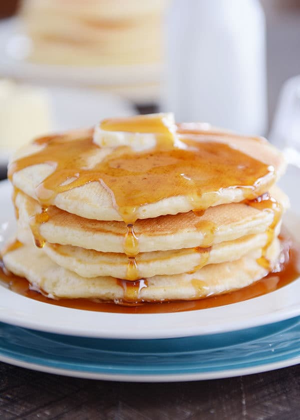 A stack of four pancakes with syrup on top and dripping down the sides and a pat of butter on top.