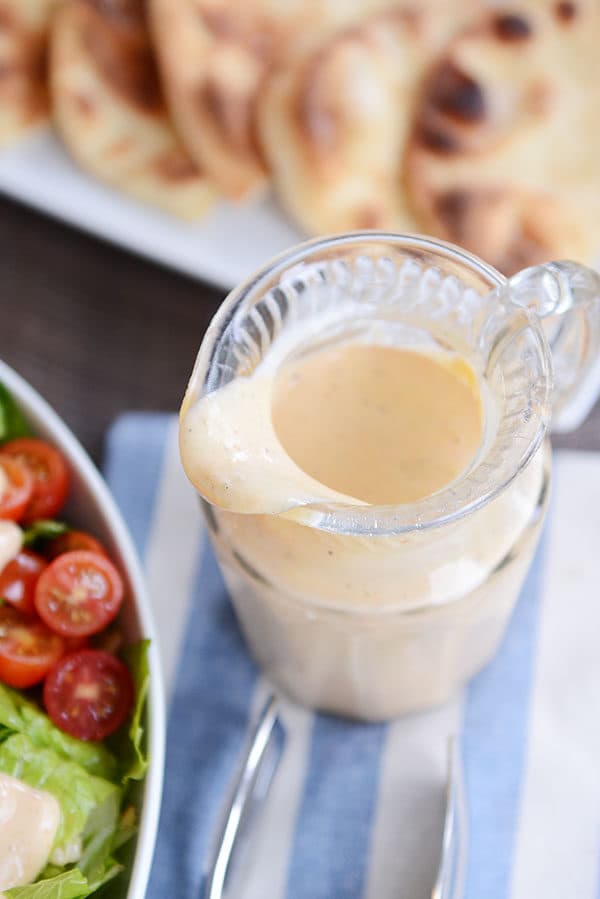 Top view of a glass pitcher of honey mustard dressing next to a plate of flatbread.