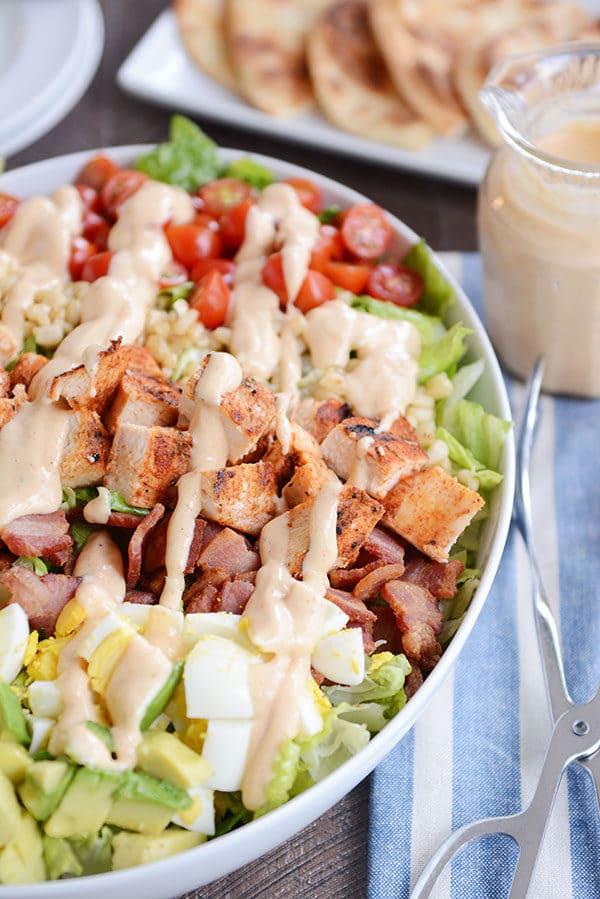 A white oval bowl full of grilled chicken cobb salad drizzled with a honey mustard dressing.