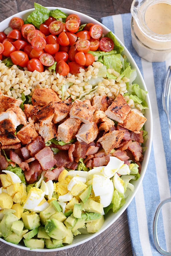 Top view of a bowl of diced avocado, diced egg, bacon, grilled chicken pieces, rice, and chopped tomatoes.