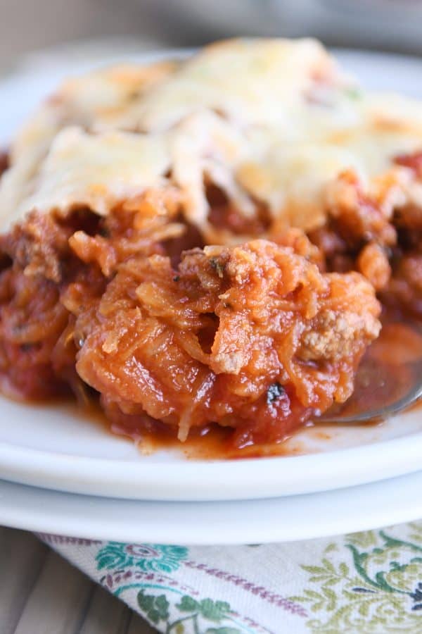 Close up of a forkful of spaghetti squash spaghetti bake topped with cheese on a white plate.