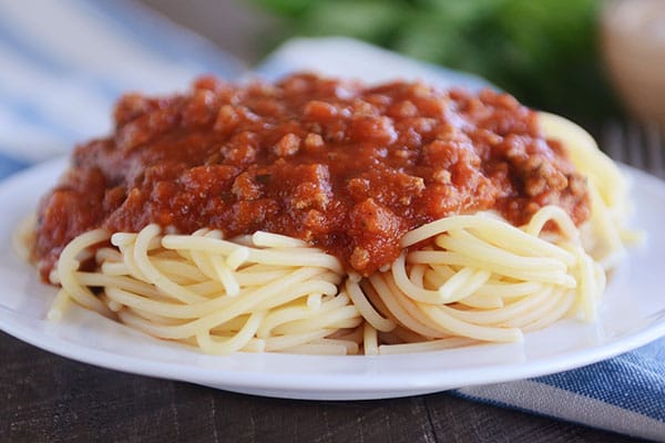 Homemade spaghetti sauce on top of cooked spaghetti noodles, filling up a big white plate
