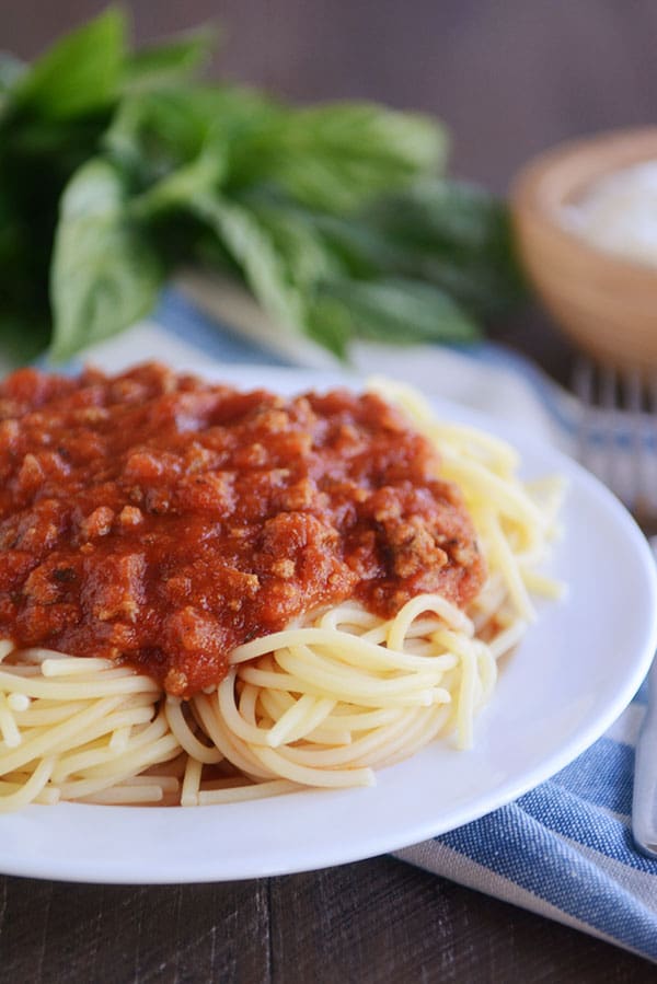 Homemade spaghetti sauce on top of cooked spaghetti noodles, all on a white plate. 