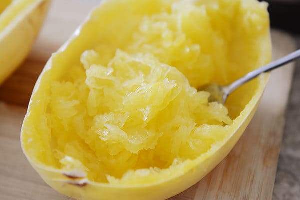 A fork taking strands of cooked spaghetti squash out of the shell. 
