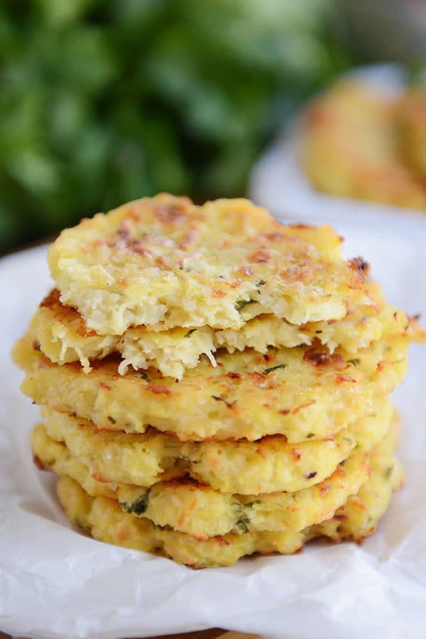 A stack of spaghetti squash parmesan fritters with the top one split in half on a piece of parchment.