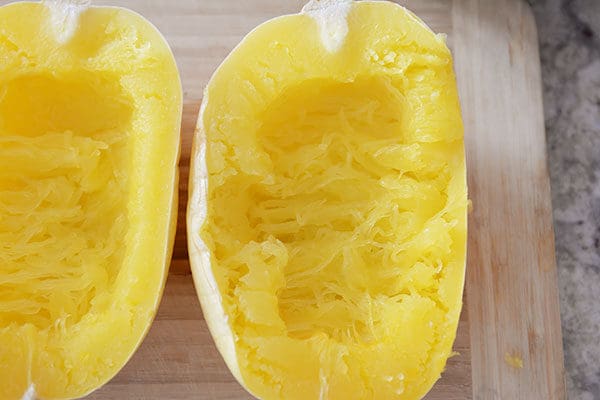 A cooked spaghetti squash cut in half sitting side by side on a wooden cutting board.