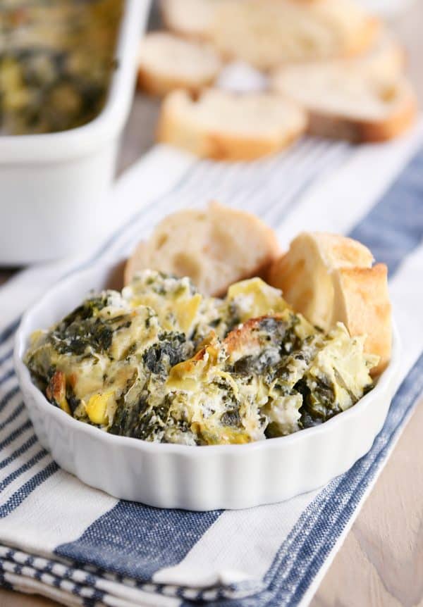 The best spinach artichoke dip in white dish with bread slices.