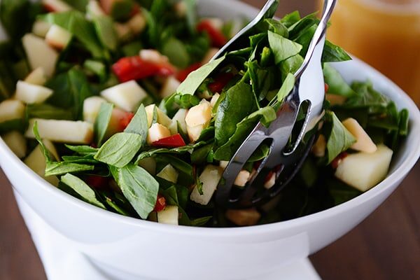 White bowl of chopped spinach and gouda salad with tongs taking a scoop out.