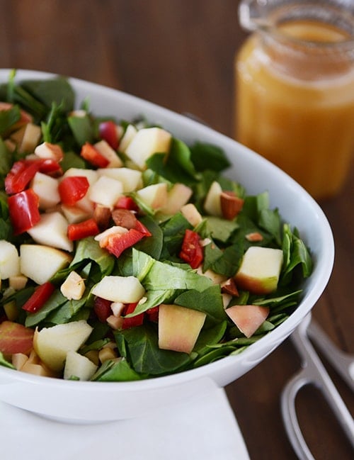 A white bowl full of chopped spinach salad with gouda, apples, and peppers. 