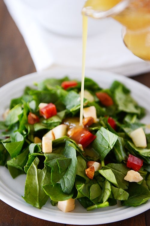 A white plate with chopped spinach salad with dressing getting poured over the top. 