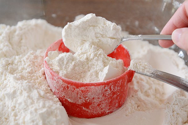 A spoon scooping flour into a red measuring cup. 