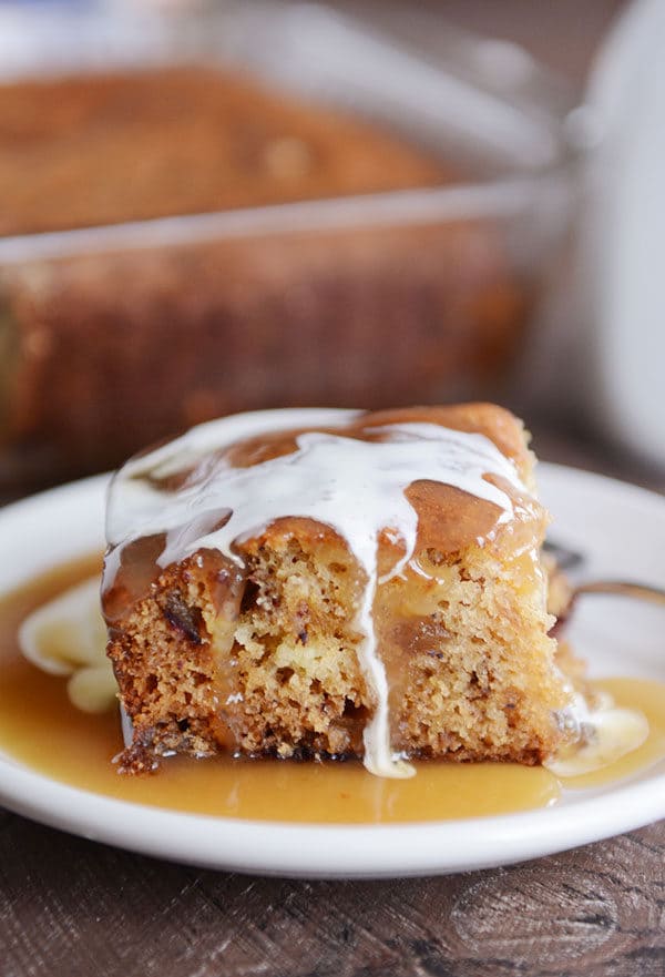 A piece of cake with light brown sauce and cream around and top of the cake.