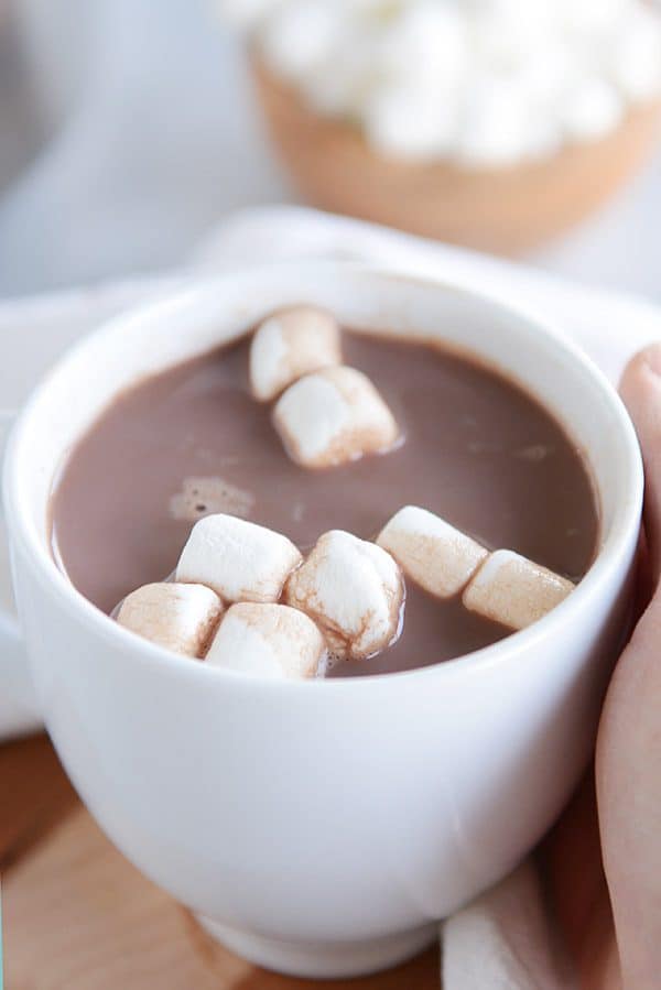 A white mug of steaming hot chocolate and marshmallows floating on the top.