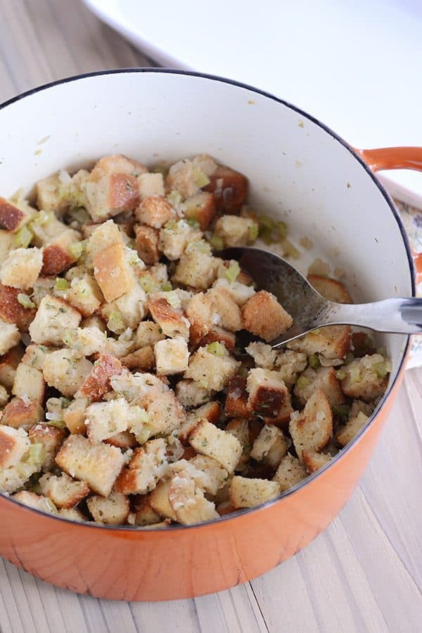 A large metal spoon taking a scoop of stuffing out of an orange pot.