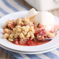White plate with scoop of strawberry rhubarb crumble and vanilla ice cream.