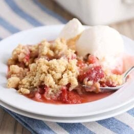 White plate with scoop of strawberry rhubarb crumble and vanilla ice cream.