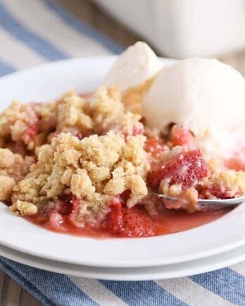 White plate with scoop of strawberry rhubarb crumble and vanilla ice cream.