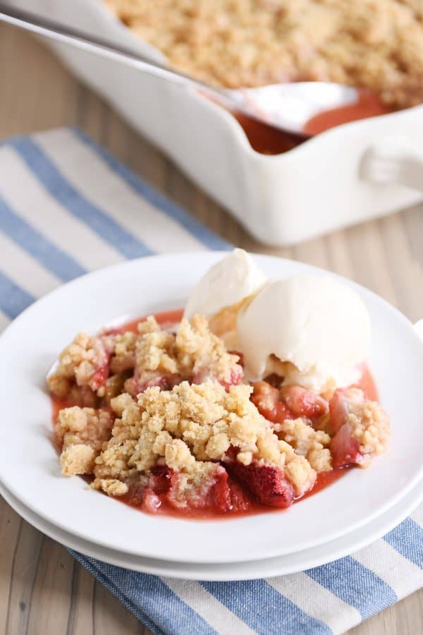 White plate with scoop of strawberry rhubarb crumble and vanilla ice cream.