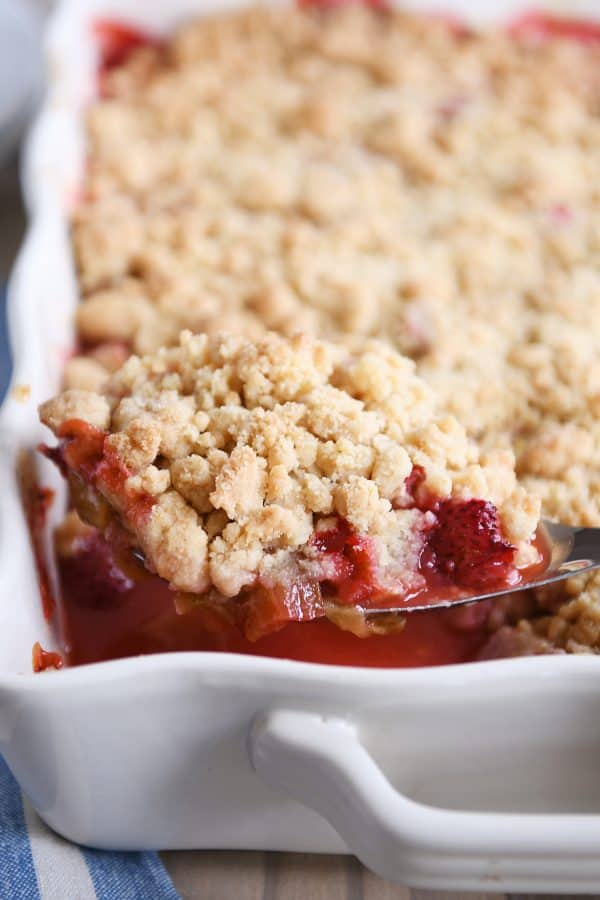 Scoop of strawberry rhubarb crumble in white baking pan.