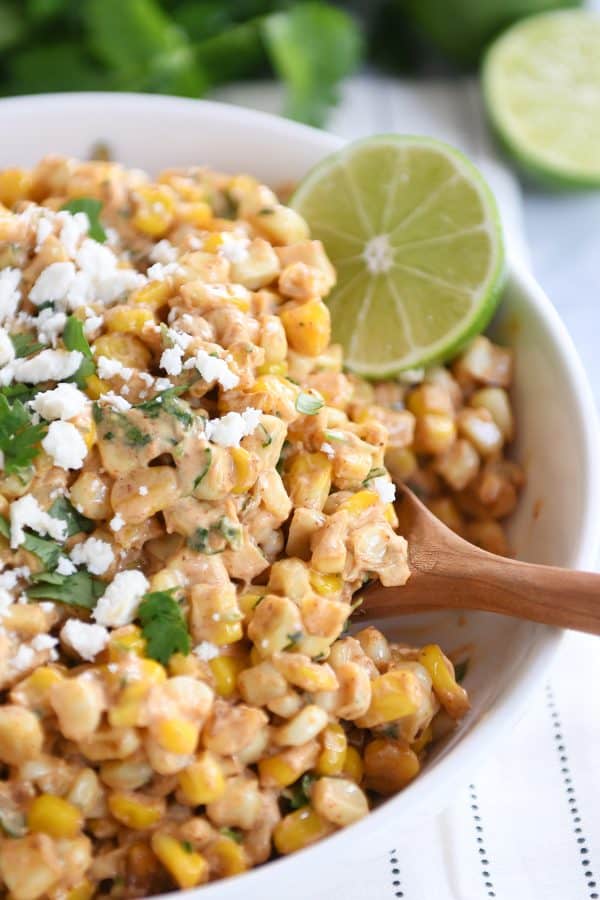 Mexican street corn salad, chopped cilantro, lime with wooden spoon.