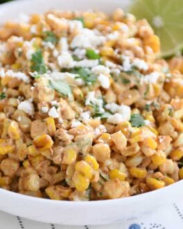 White bowl filled with Mexican street corn salad, topped with cilantro and lime.