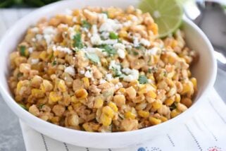 White bowl filled with Mexican street corn salad, topped with cilantro and lime.