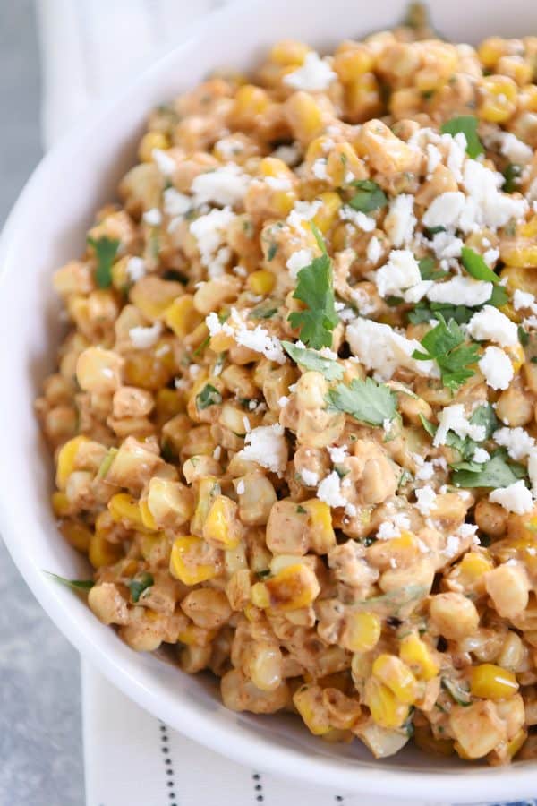 White bowl filled with Mexican street corn salad, topped with cilantro and lime.