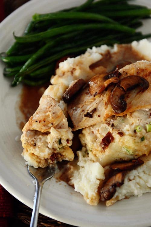 Stuffed chicken breast on a bed of mashed potatoes, next to a serving of green beans.