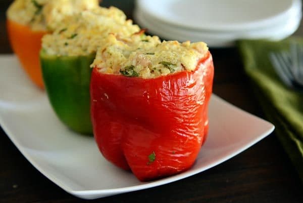 An orange, green, and red stuffed pepper lined up on a white platter.