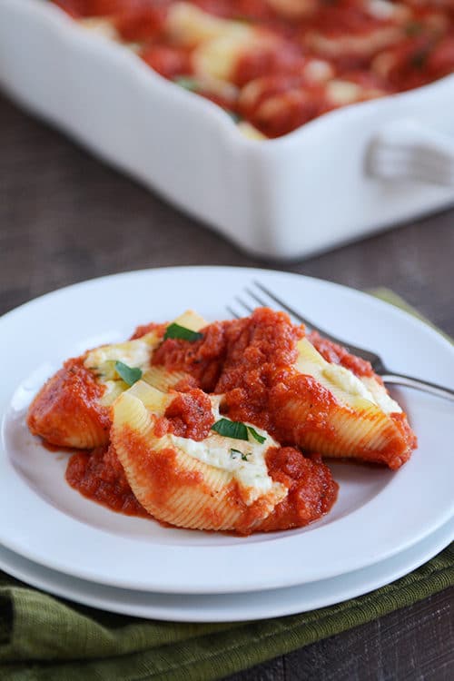 Three ricotta cheese-stuffed pasta shells topped with red sauce, on a white plate. 