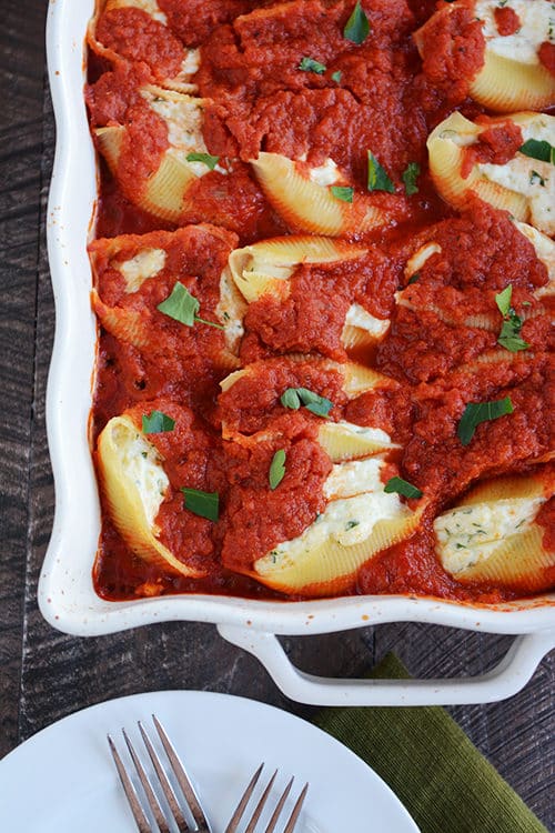 A casserole dish filled with cheesy pasta shells, and topped with red sauce and sprinkled parsley.