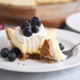 Berries and cream pie on a white plate with a bite taken out.