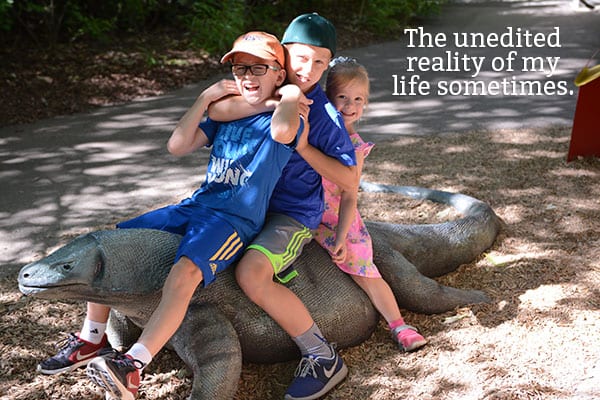 Three children sitting on a stone lizard.
