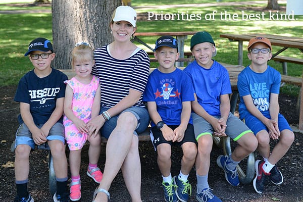 A mother and five kids sitting on a picnic bench.