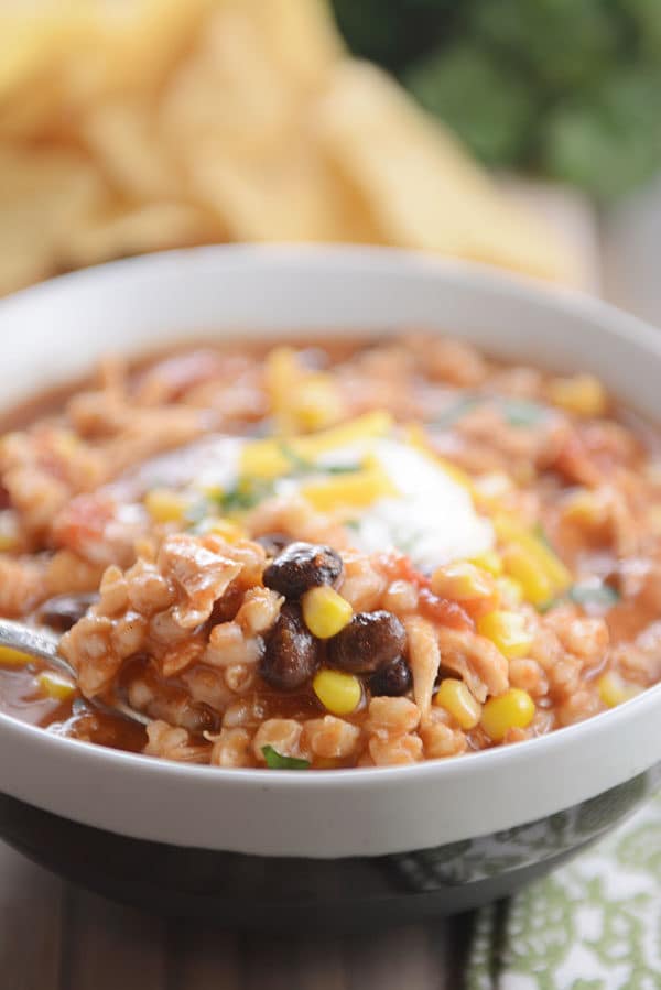 A spoon taking a big bite of southwestern chili out of a white bowl.