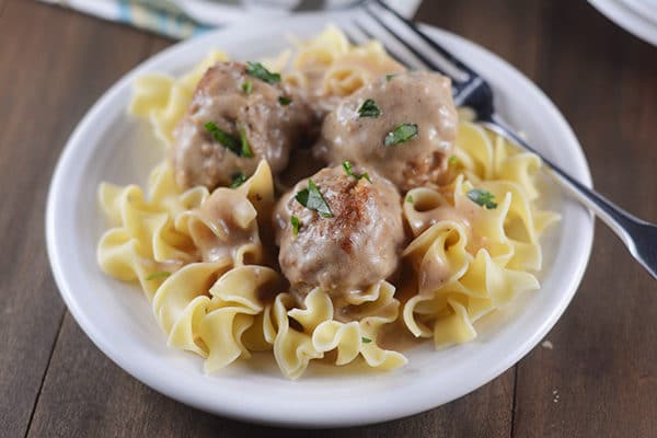 A white plate with cooked egg noodles and three Swedish meatballs.