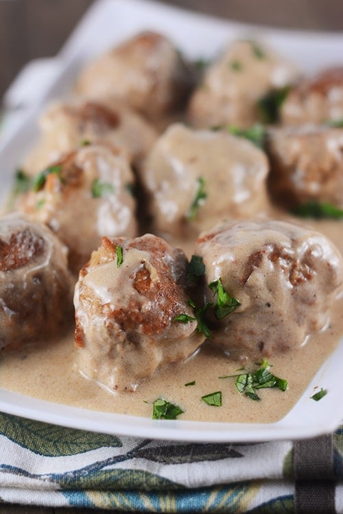 A white platter of golden brown cooked meatballs and gravy. 
