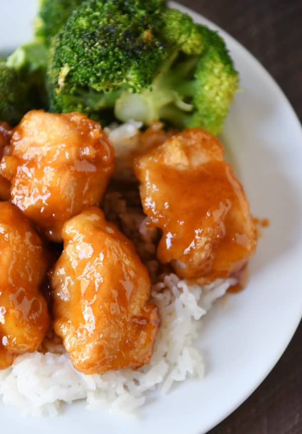 Top down view of baked sweet and sour chicken over rice on white plate.