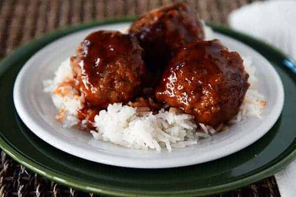 sweet and sour meatballs over white rice on a white plate