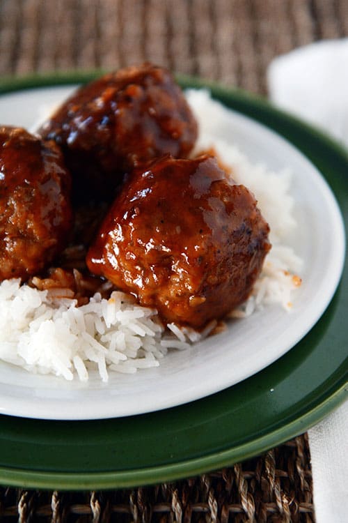 Several meatballs covered with sweet and sour sauce on white rice.