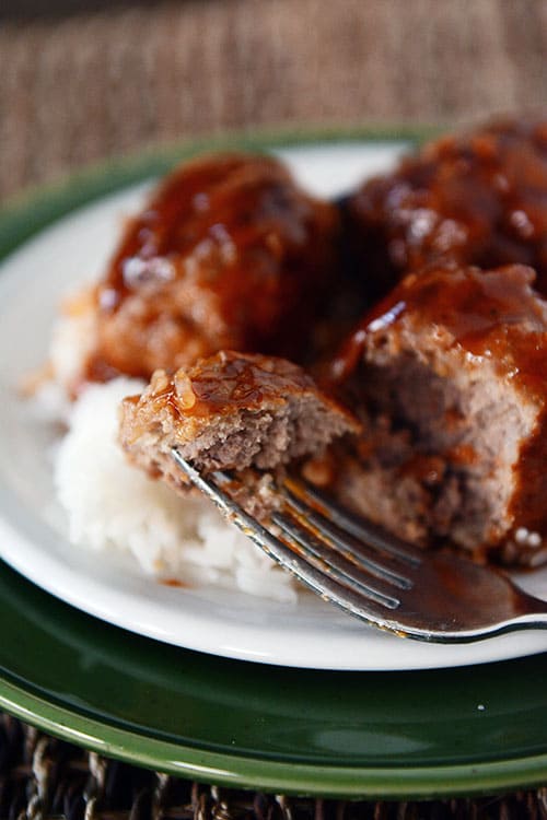 Sweet and sour meatballs over white rice with one meatball getting a bite taken out.